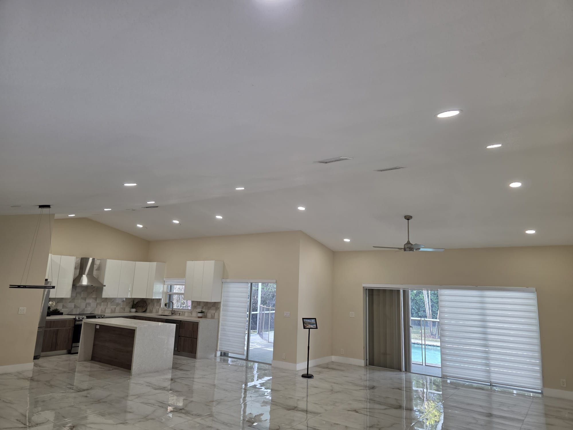 Open-concept kitchen and living room with vaulted recessed lighting and black linear pendant over an island.