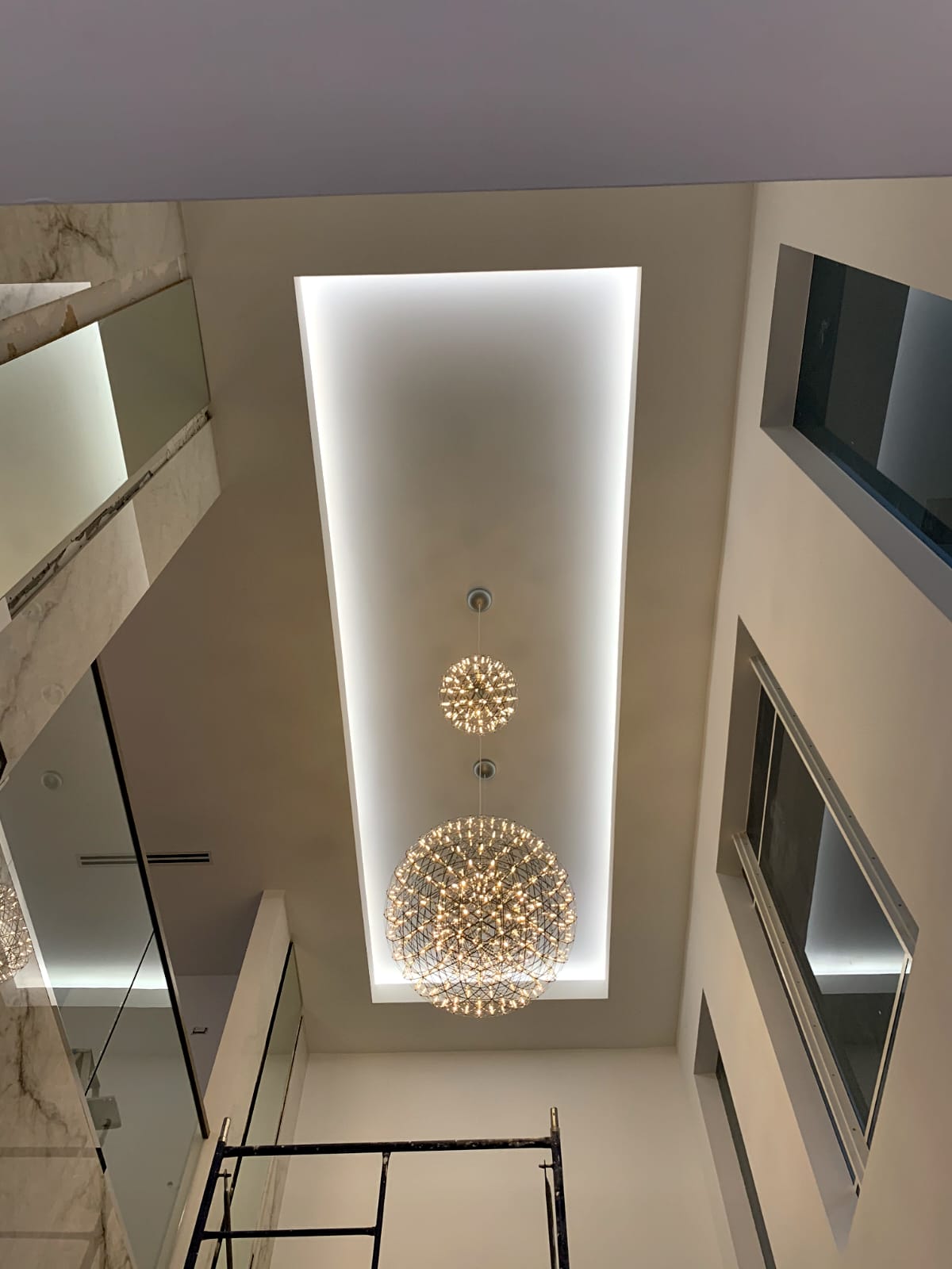 Low-angle view of two spherical LED chandeliers in a recessed ceiling with perimeter cove lighting.